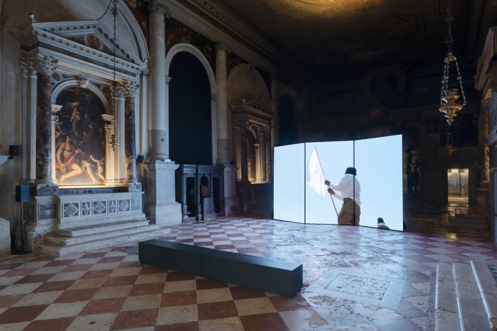 A screen showing a man holding a white flag, installed in a 16th-century cathedral at an event by the Fondazione In Between Art Film