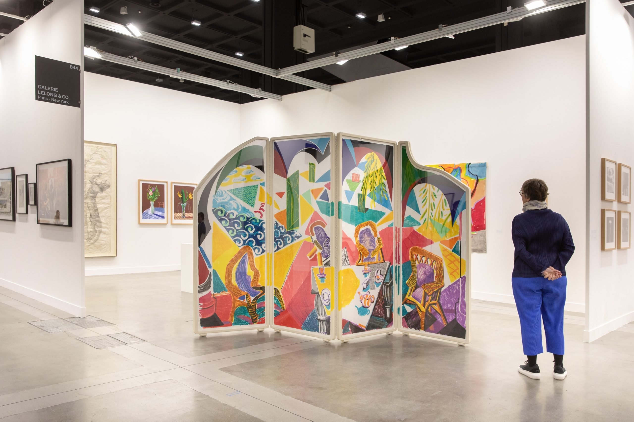 A colorful folding screen is seen in a color photo of a white-walled booth.