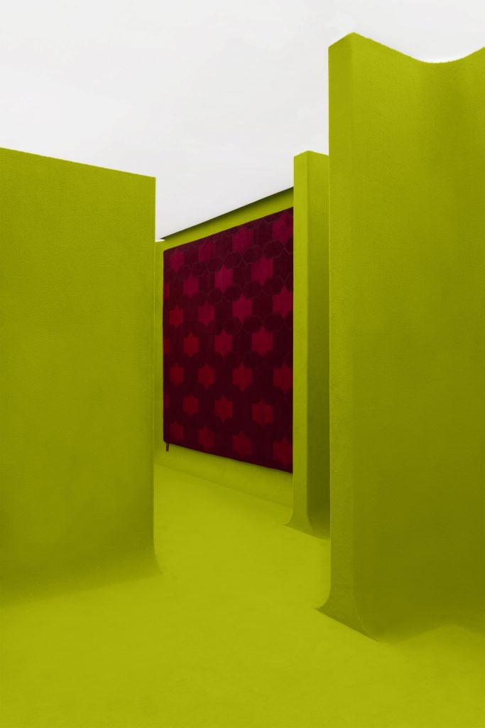 a blood red designer rug hangs on a wall of an acid green maze 