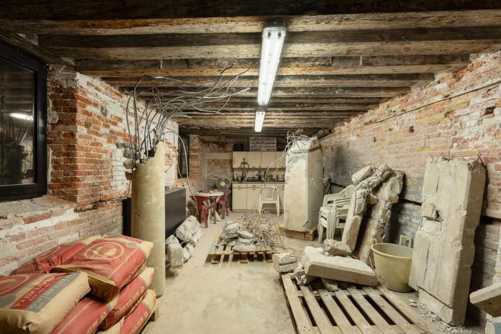 a wooden basement room that is dusty and has sand bags and old plastic chairs and fans