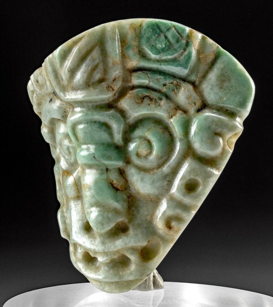A jade carving of a human face with intricate designs, likely representing a deity or high-status individual. This artifact is characteristic of the Olmec civilization, known for its colossal heads and jade carvings.