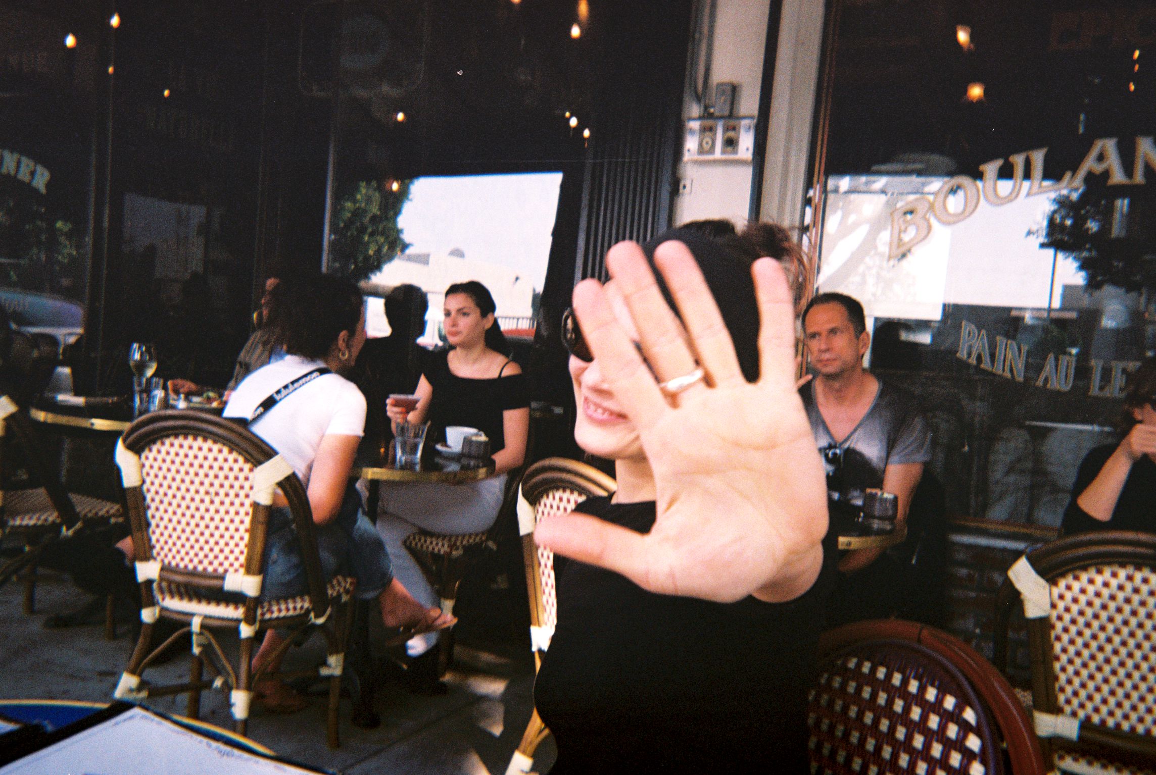 A woman blocks a photo of herself taken at an outdoor brasserie.