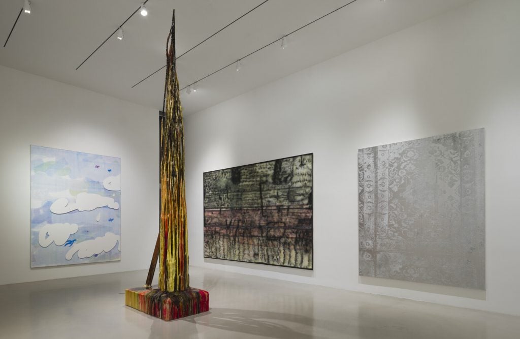 Three abstract paintings and one large vertical sculpture in a gallery