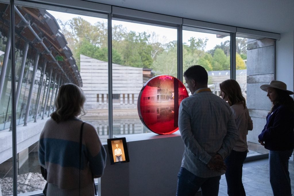 several people stand in front a red circular sculpture in a museum