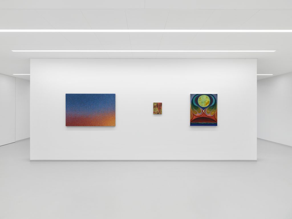 Three abstract paintings on the wall of a white cube gallery space with three rows of lights along the ceiling.