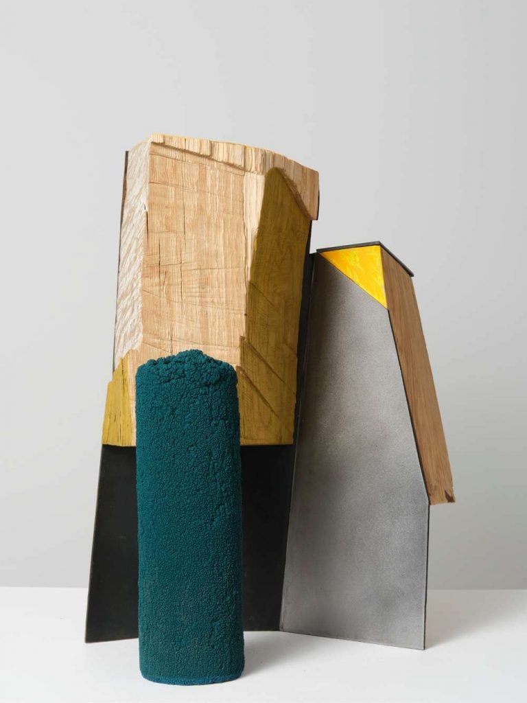 A sculpture made of wood and metal is painted with green, yellow and silver