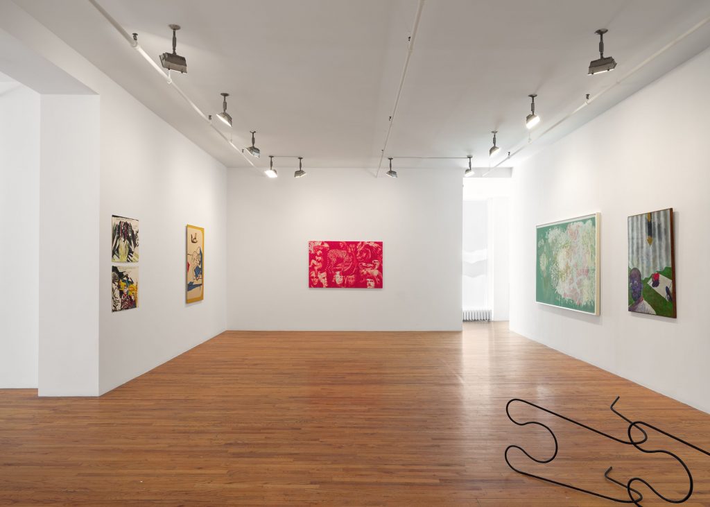 A white-walled gallery with a wood floor contains a number of artworks in this color photo
