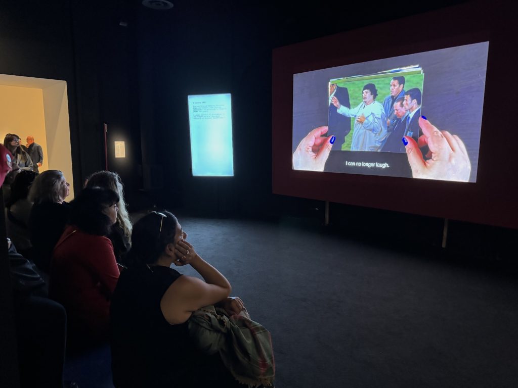 A film plays showing a picture of two hands manipulating a photo as an audience looks on