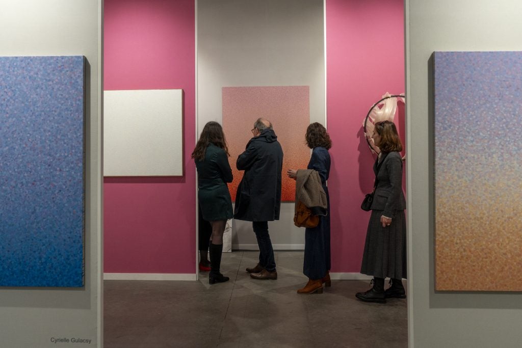 a group of people viewing artworks on the wall, in pink, blue and soothing colours.