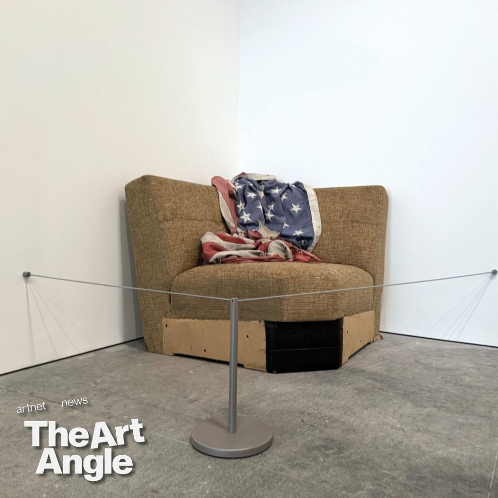 an old brown sofa draped in a dirty and faded american flag is cordoned off in a corner of the gallery
