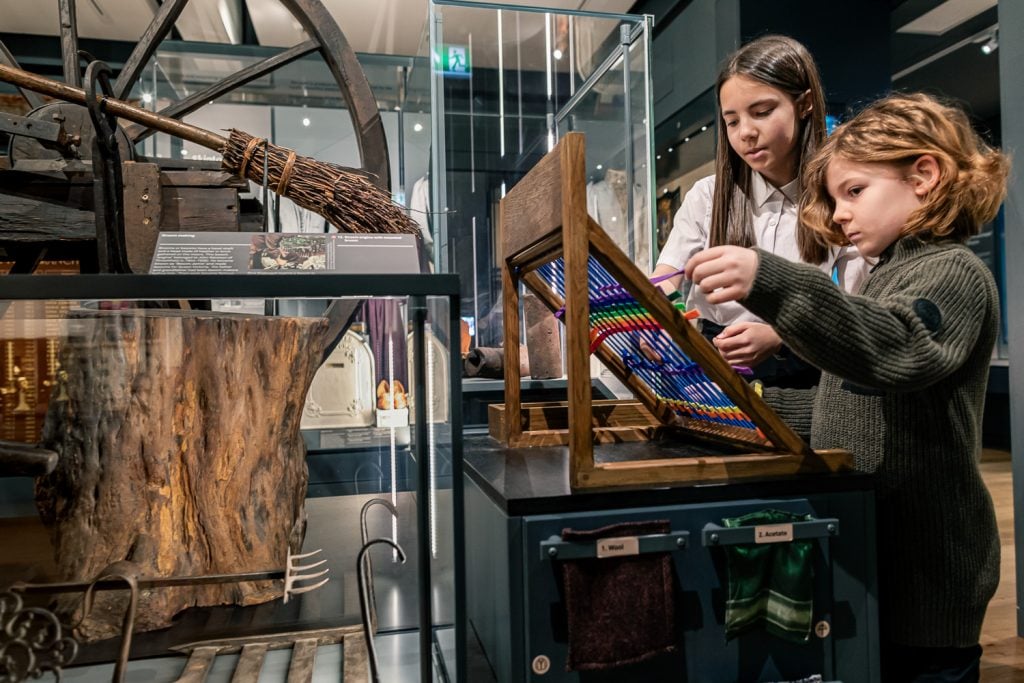 Two children look at a display of colourful embroidery in a museum