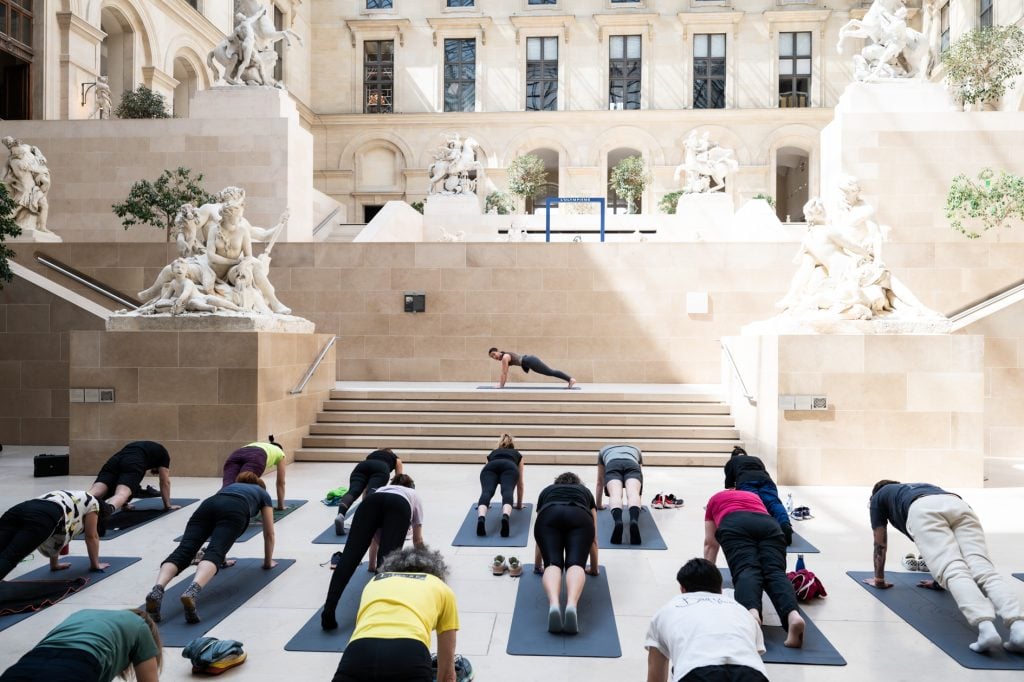 people perform yoga inside the Louvre