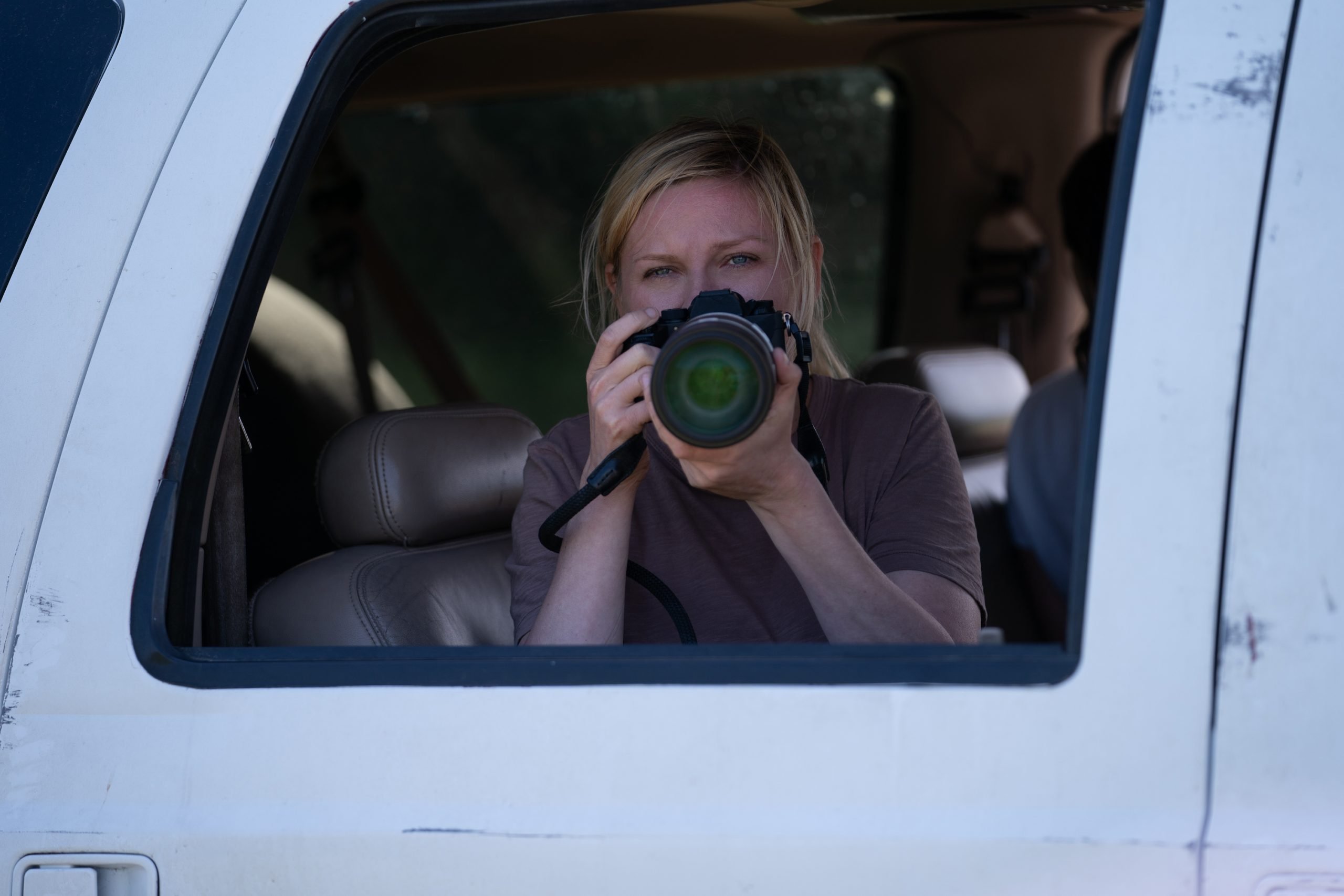 A still from the movie "Civil War," showing a woman in a car holding a camera