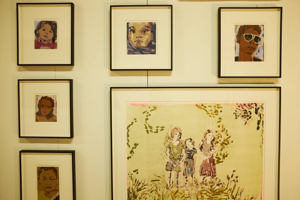 a yellow wall with small framed portraits hanging in a loose grid formation