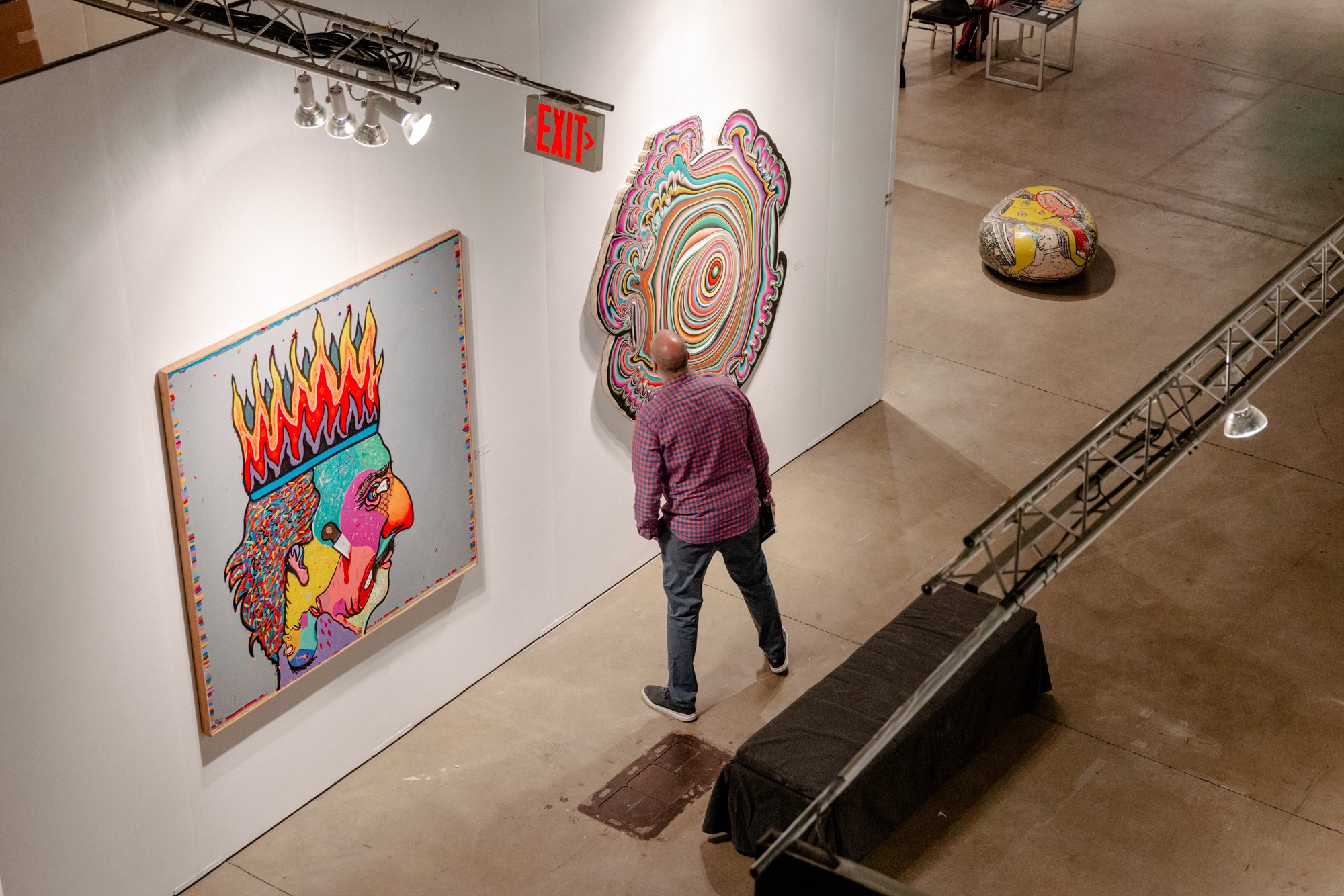 An image of a visitor looking at two paintings on the wall of a booth at an art fair