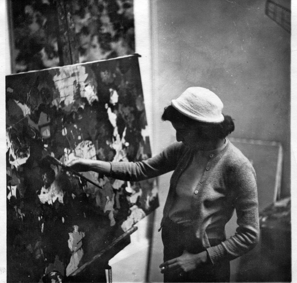A black-and-white photo of a young Flack painting an abstract expressionist style painting while holding a cigarette.