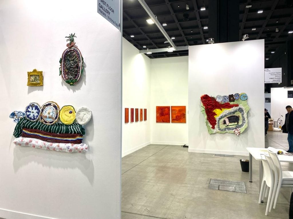 A white-walled booth shows artworks of a variety of colors and shapes—perhaps made of fabric