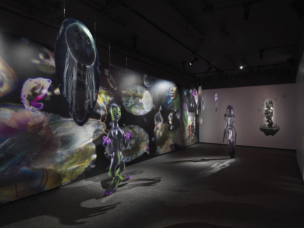 an immersive gallery space with projections on the wall and sculptures suspended from the ceiling