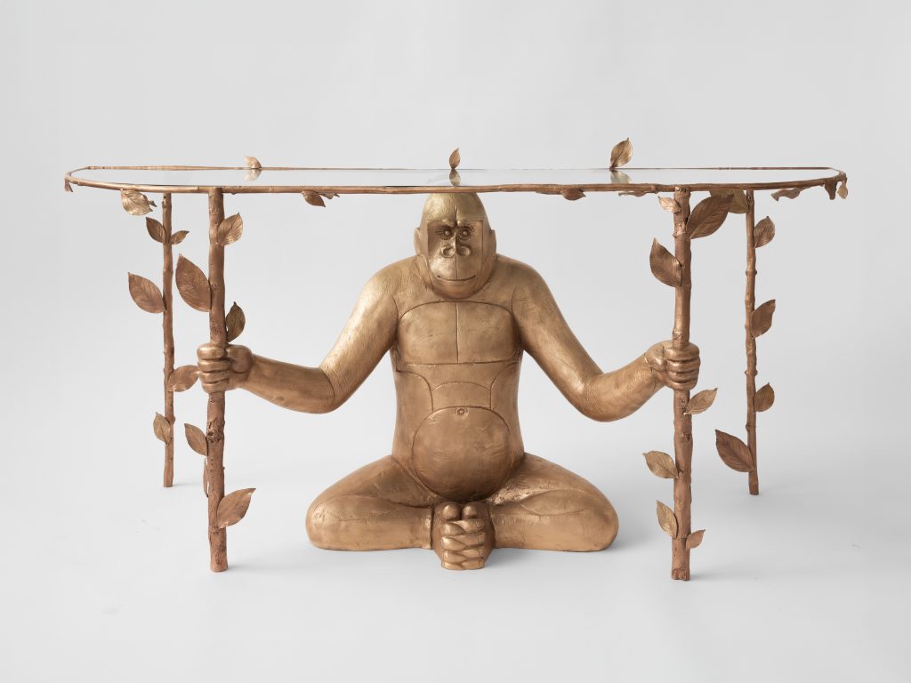 A surreal table looks like a gorilla holding leafed vines with a glass top