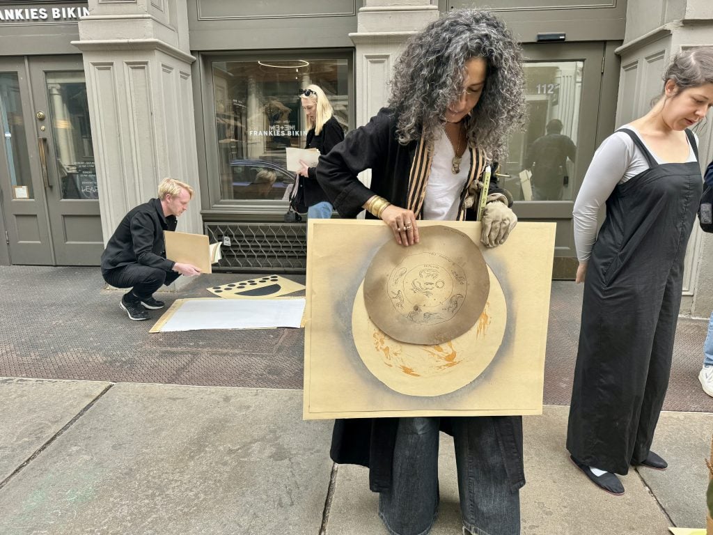 A woman on the street holds up a large drawing of the moon.