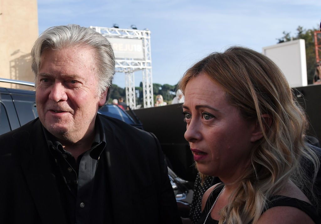 The image features a man and a woman, identified as Steve Bannon and Georgia Meloni. They are outdoors, and both are wearing jackets. The background includes the sky.