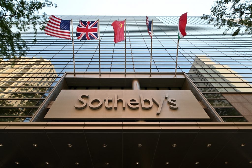 the exterior of sotheby's in new york. the building is tall and made of glass with multiple flags outside