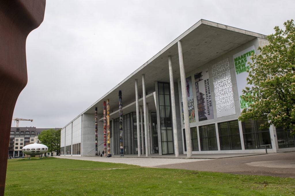The image shows the Pinakothek der Moderne with columns and a grass lawn. The text in the content seems unrelated to the image. The location appears to be in Munich, with tags including outdoor, sky, grass, building, and architecture.
