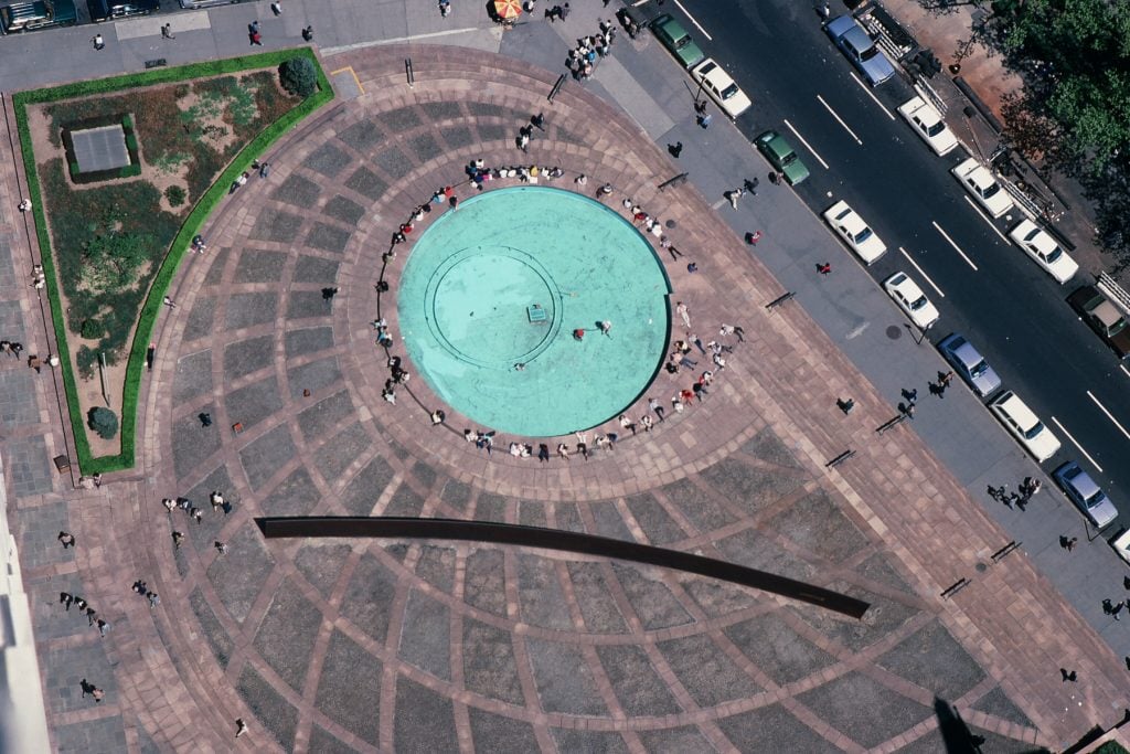 an aerial photo of a urban plaza, a picture of an empty fountain and a long sculpture that curves across the plaza