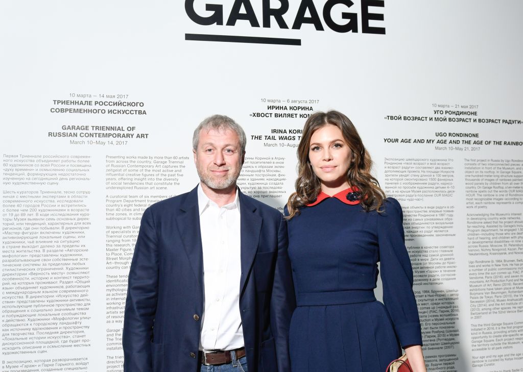 The image shows a man and a woman posing for a picture, identified as Roman Abramovich and Dasha Zhukova. They are at the Garage Triennial of Russian Contemporary Art exhibition.