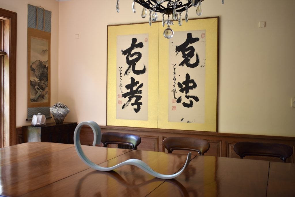 A pair of Japanese ink calligraphy hung on the wall, in front there's an abstract sculpture standing on a stable