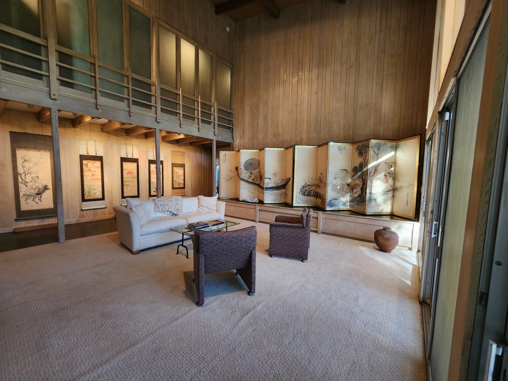 The view of a large room where sofa and seats are place in the middle, and the walls are full of panels and scrolls of Japanese ink art.