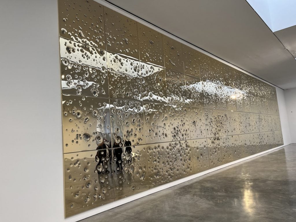 A long row of golden panels is seen on a white wall in a photo.