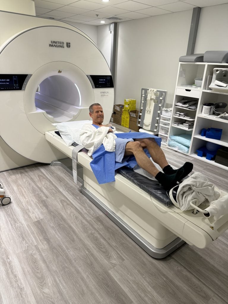 A man in hospital garb enters an cylindrical MRI machine in a color photo