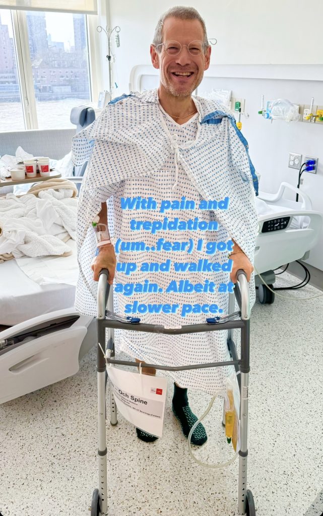 A man in a hospital gown stands behind a walker