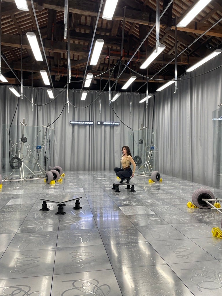 woman squats on a steel stage that is lined with silver curtains 