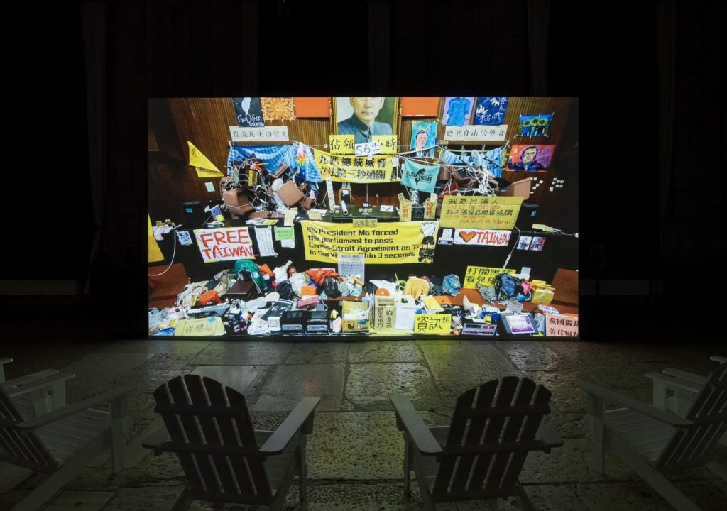 a video of a protest in Taiwan on a large screen in a dark viewing room 