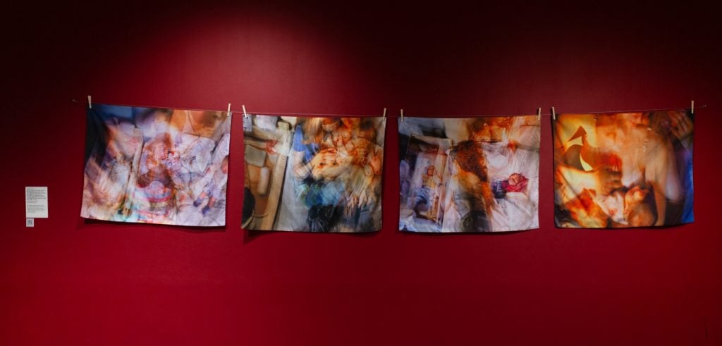 four colourful semi-abstract textiles hanging on a red wall