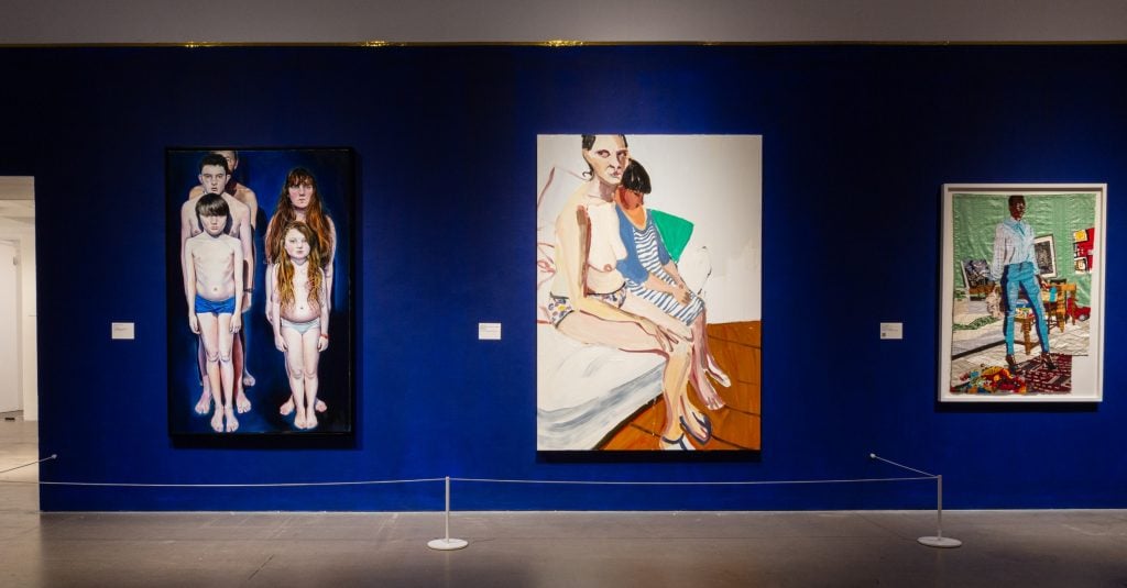 three figurative paintings depicting figures hanging on a blue wall