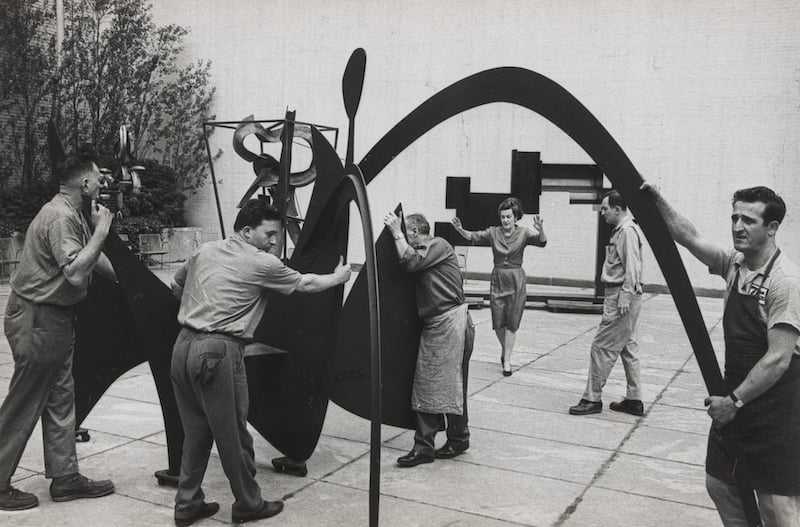 A black and white photo of a team stationing a sculpture while a woman gesticulates, providing energetic guidance