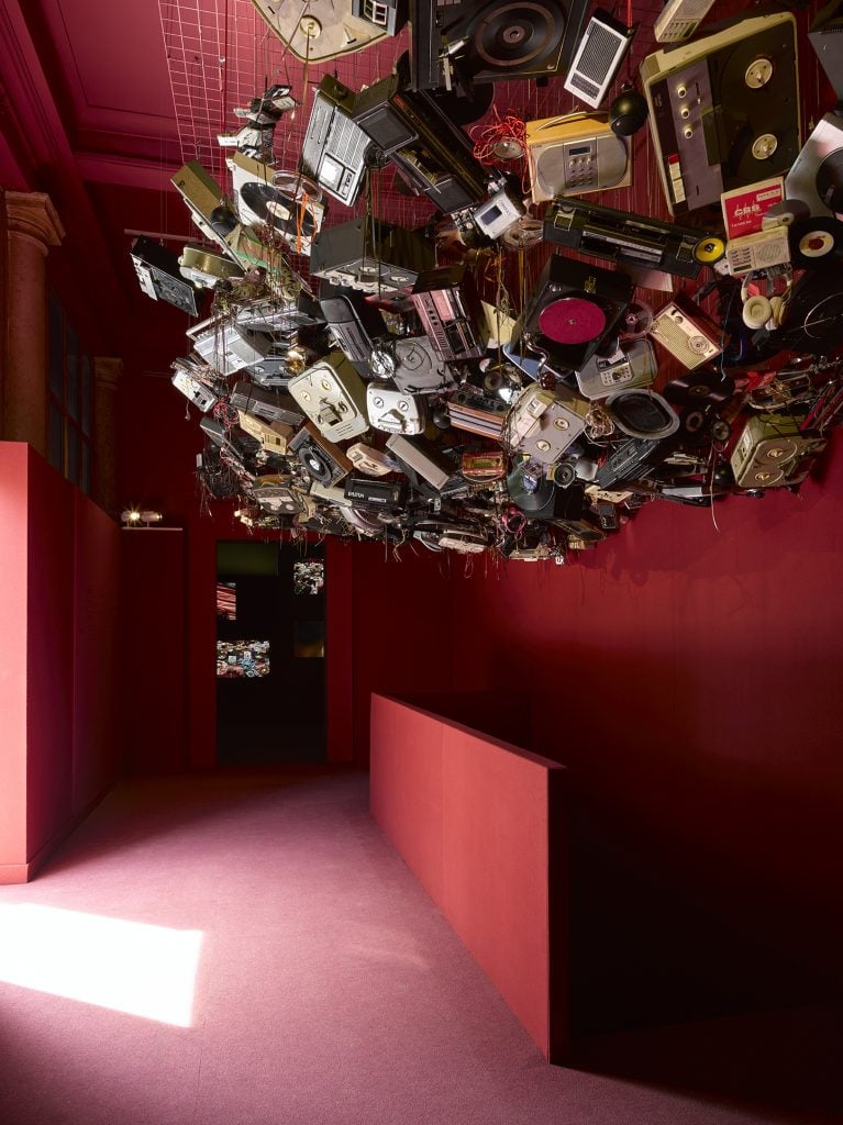 A bunch of video and audio players are bundled on the ceiling of a red room.
