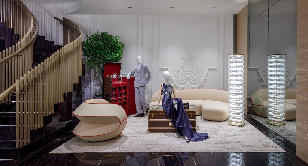 Two mannequins in glamorous evening wear are positioned next to modern luxury furniture.