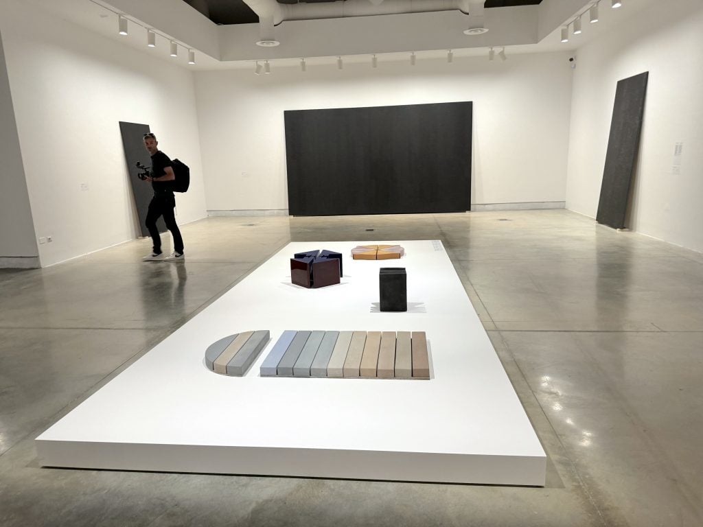 A series of ceramic objects on the ground, with black paintings leaned against the wall behind