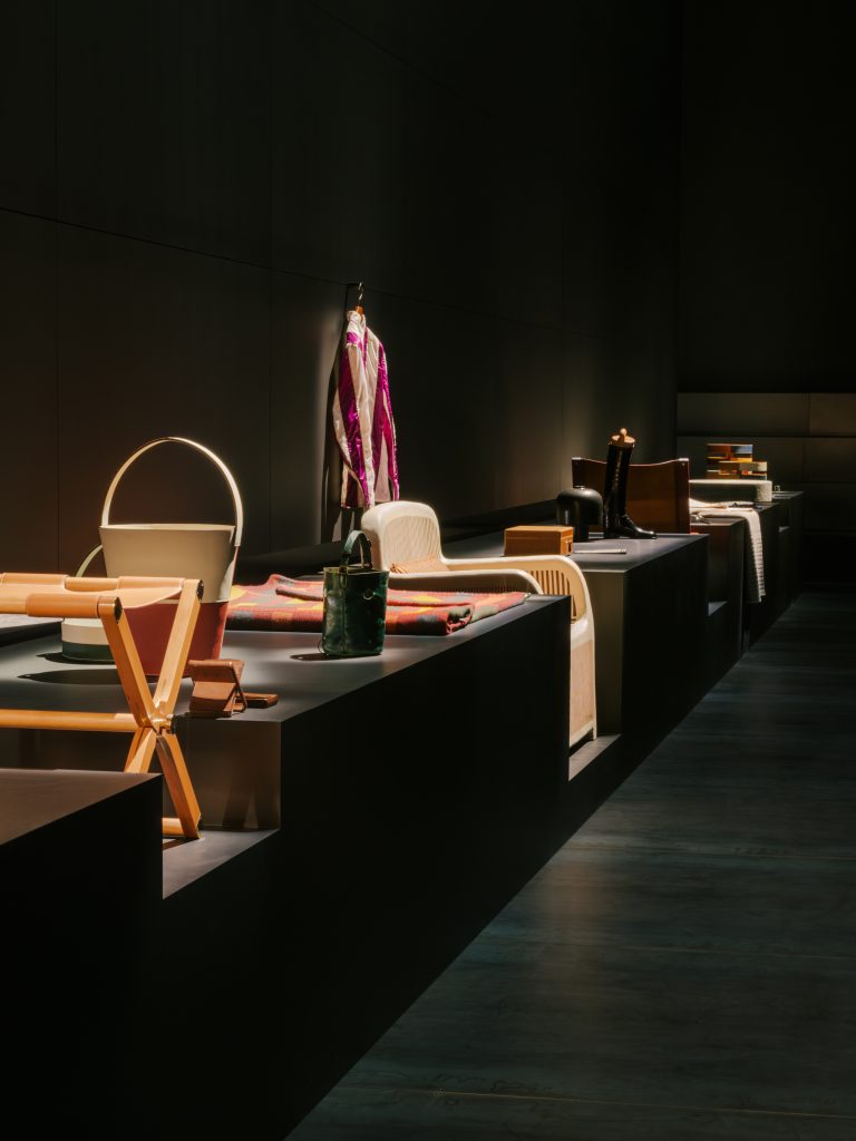 an array of leather goods is arranged in a dark gallery 
