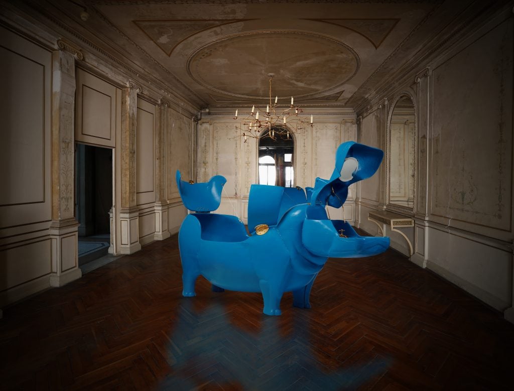 a large shiny royal blue sculpture of a hippopotamus is in a bare room 