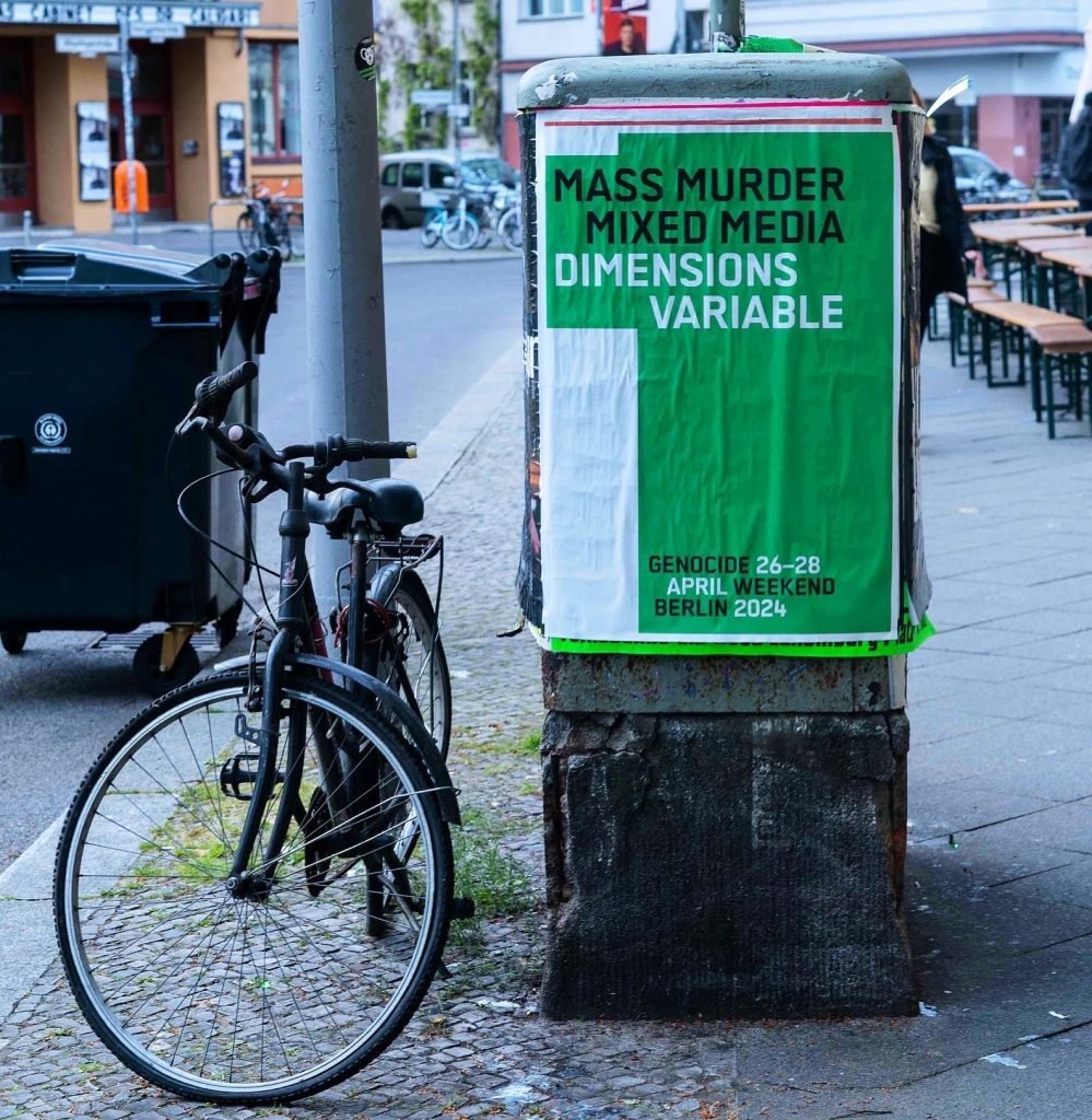 a poster is posed on the street in Berlin, you can also see a lamppost, a bike and a bin