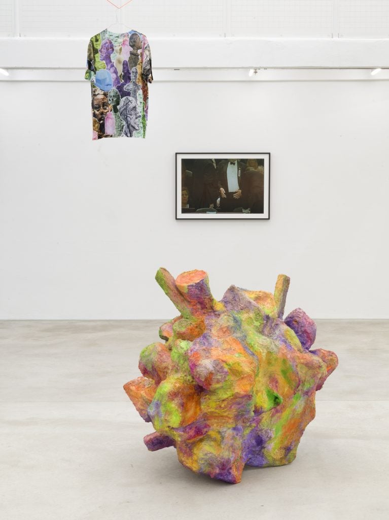 an art installation in a white gallery that includes a shirt, a sculpture, and a photograph