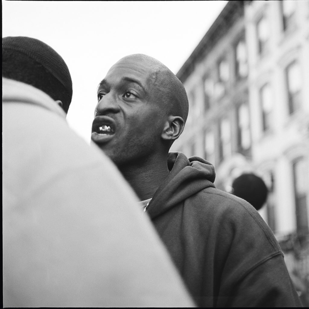 Black and white portrait of a man, rapper Rakim, leaning in to speak to another man.