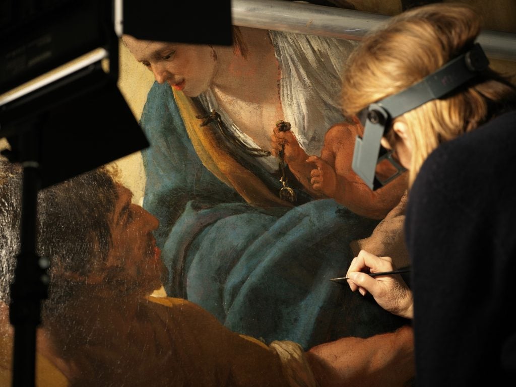 A woman holding a paintbrush to restore a historic painting, which was rescued from a fire at the Notre-Dame cathedral