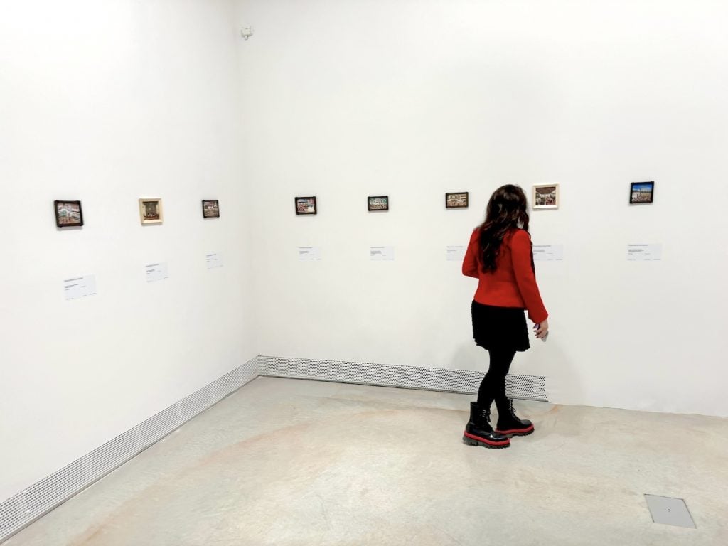 A gallerygoer looks at a row of small paintings