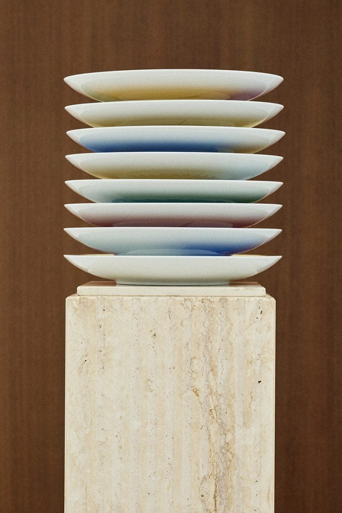 Designer porcelain dishes are stacked atop a marble plinth.